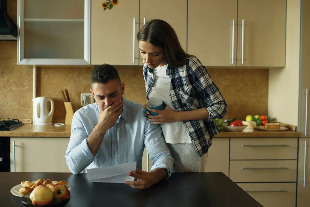 A couple at a kitchen table reading a bill together.